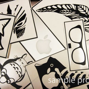 May include: A collection of black and white stickers featuring various designs, including an apple logo, a butterfly, a pair of glasses, a cartoon creature, and a shoe. The stickers are printed on a white background.