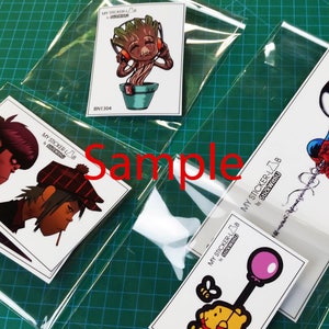 May include: Four clear plastic bags with different sticker designs. The stickers feature characters from popular movies and TV shows, including a green tree-like creature with headphones, a red and blue superhero, and a cartoon character with a red hat. The text on the bags reads "My Sticker Lab" and "Stick With U".