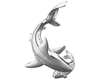 以下が含まれることがあります： 銀色のサメのペンダント。口に魚をくわえています。サメは躍動感のあるポーズで、背びれが立っています。ペンダントはおそらく金属製で、研磨仕上げです。