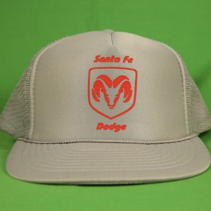 May include: A gray and white mesh trucker hat with a red embroidered Dodge logo and the text "Santa Fe" above it.