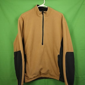 May include: A brown fleece pullover with black accents on the sleeves and pockets. The pullover has a quarter-zip closure.