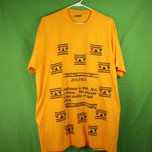 May include: Yellow t-shirt with a black and green geometric pattern and the text "JUS-TICE: Conformity to truth, fact, or reason. The principle of just dealing or right action."