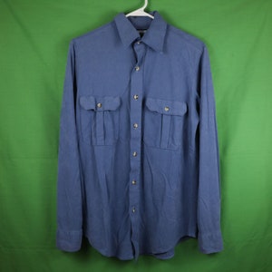 May include: A blue long-sleeved button-down shirt with two large flap pockets on the front.