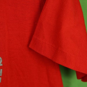 Op de afbeelding: Rood T-shirt met een zilveren afbeelding met de tekst "In Culture" aan de linkerkant.