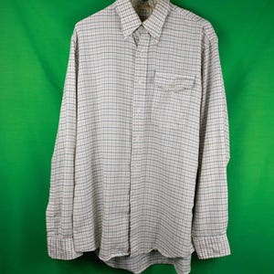 May include: A long-sleeved button-down shirt with a checkered pattern in white, blue, and red. The shirt has a collar, a chest pocket, and buttoned cuffs. It is hanging on a white hanger against a green background.