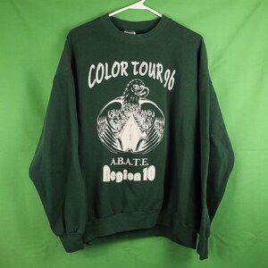 May include: A dark green sweatshirt with white text and graphics. The front features the words "COLOR TOUR 96" above an eagle design and the text "A.B.A.T.E. Region 10" below. The sweatshirt has long sleeves and a crew neck.