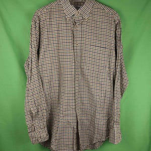 May include: A long-sleeved button-down shirt with a checkered pattern in brown, navy, and white. The shirt has a button-down collar, a chest pocket, and buttoned cuffs. The shirt is hanging on a white hanger against a green background.