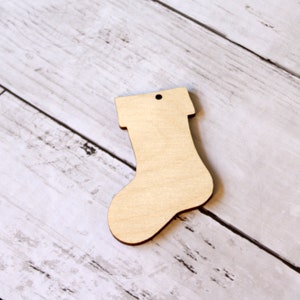 May include: A plain wooden Christmas stocking ornament with a hole at the top for hanging.
