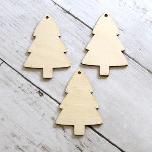 May include: Three unfinished wooden Christmas tree decorations. The decorations are shaped like a traditional Christmas tree and have a hole at the top for hanging.