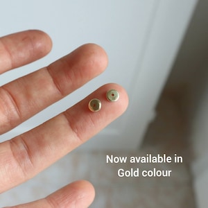 May include: Two small, round, gold-colored metal components with a hole in the center. The text "Now available in Gold colour" is visible in the image. These components are likely jewelry findings or small decorative elements.