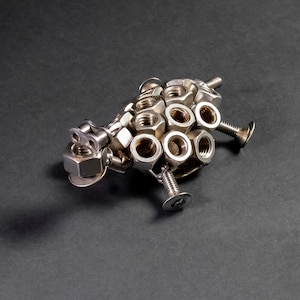 May include: A silver metal sculpture of a sheep made from nuts and bolts.