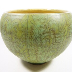 May include: A green ceramic bowl with a textured, wood-grain pattern. The bowl has a rounded shape and a slightly flared rim.