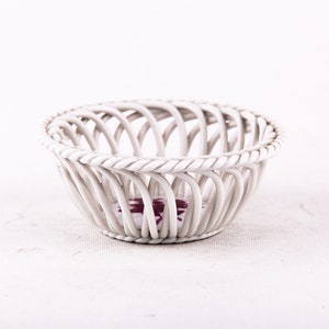 May include: White ceramic basket with a woven design. The basket is empty and has a small purple design on the bottom.