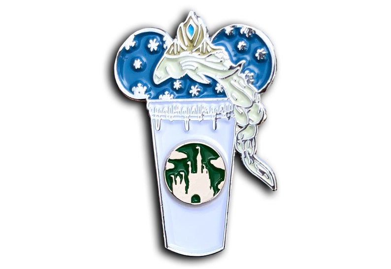 May include: A white enamel pin with a blue and white Mickey Mouse ear design. The ears are filled with snowflakes and a white figure with a blue crown and a white braid is inside the ears. The figure is holding a white cup with a green Starbucks logo and a green castle inside the logo. The cup has white icing dripping down the sides.
