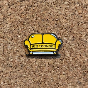 May include: Yellow enamel pin shaped like a sofa with the text "PIN LOUNGE" on the front.