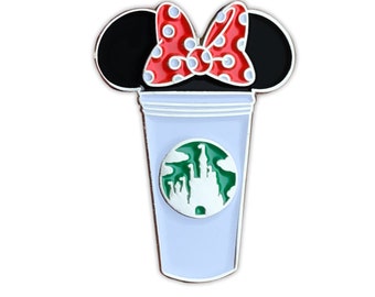 Può includere: Una tazza di caffè bianca con un logo di castello verde e bianco. La tazza ha un fiocco rosso con pois bianchi in cima, che ricorda le orecchie di Topolino.