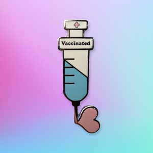 May include: A silver enamel pin shaped like a syringe with a pink heart at the end. The syringe is filled with blue and white liquid and has the word "Vaccinated" on the side.