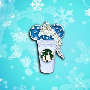 May include: A blue and white enamel pin featuring a stylized image of Elsa from Frozen, with her hair frozen in a swirl, inside a coffee cup with a green logo of a castle. The cup has a white rim and a white base.