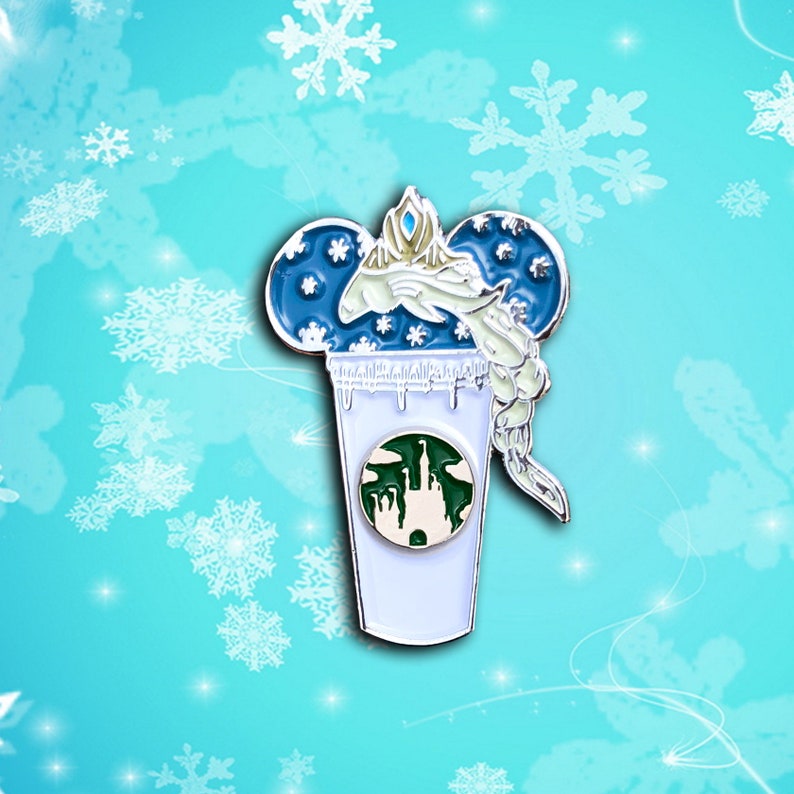 May include: A blue and white enamel pin featuring a stylized image of Elsa from Frozen, with her hair frozen in a swirl, inside a coffee cup with a green logo of a castle. The cup has a white rim and a white base.