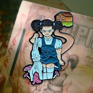 May include: A black and white enamel pin featuring a girl with pigtails holding a white rabbit. The girl is wearing a blue dress and is standing on a path leading to a small brown house. There are pink mushrooms on either side of the girl.