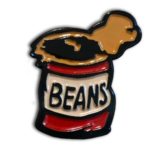 May include: A black enamel pin of a can of beans with the word "BEANS" printed on the label. The can is open and the top is bent over.