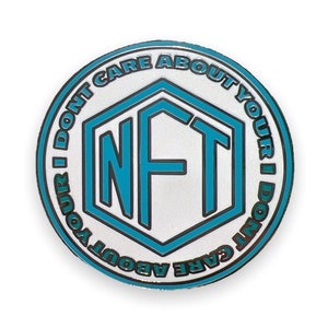 May include: A round, blue and white enamel pin with the text "I don't care about your NFT I don't care about your NFT" in a circle around a hexagon with the letters "NFT" in blue.