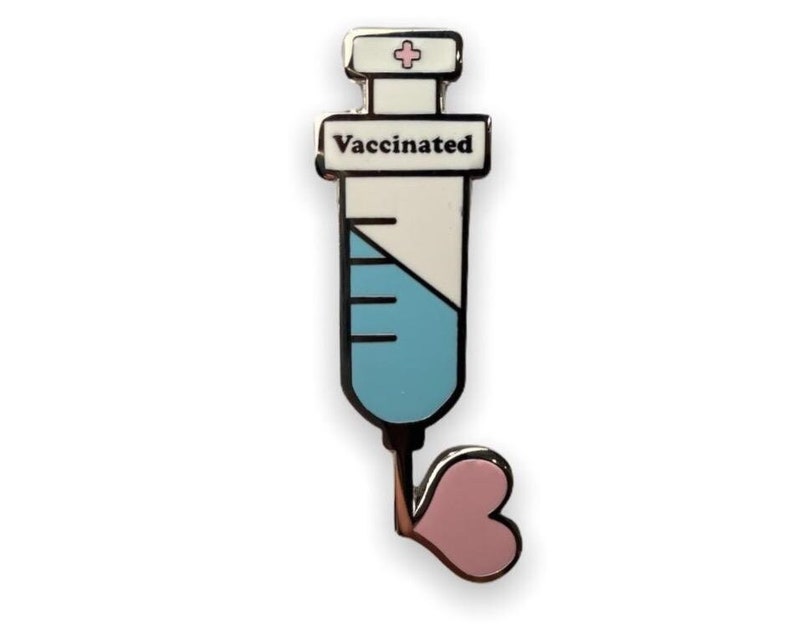 May include: A silver enamel pin shaped like a syringe with a pink heart at the end. The syringe is filled with blue liquid and has a white label that says "Vaccinated".