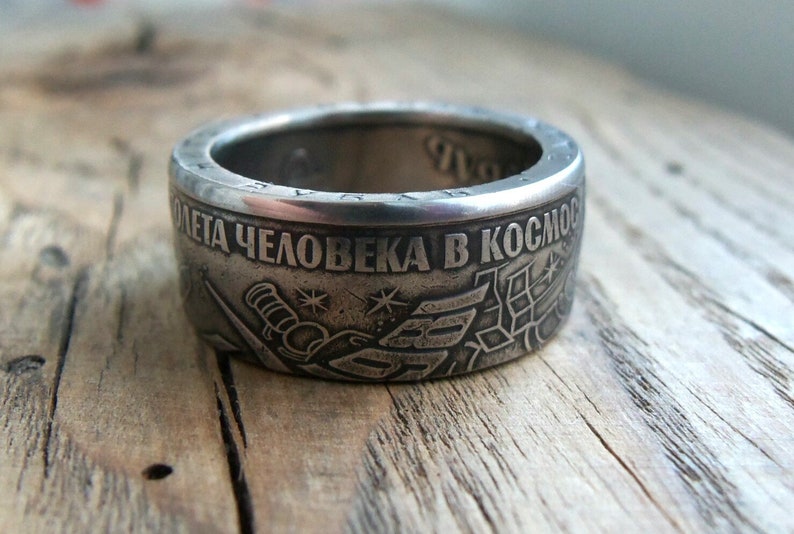 Op de afbeelding: Een zilveren ring met de inscriptie "50 лет человека в космосе" (50 jaar mens in de ruimte) en een afbeelding van een raket en sterren.
