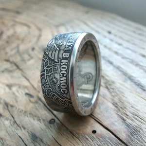 Op de afbeelding: Een zilveren ring gemaakt van een munt met de inscriptie "ПОЛЕТ ЧЕЛОВЕКА В КОСМОС" (Vlucht van de mens naar de ruimte) en een afbeelding van een raket.