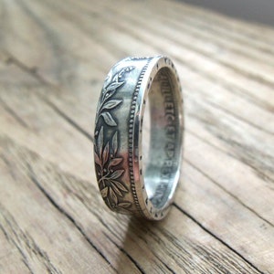 May include: Silver ring made from a vintage coin with a floral design. The ring is engraved with the words "UNITED STATES OF AMERICA".