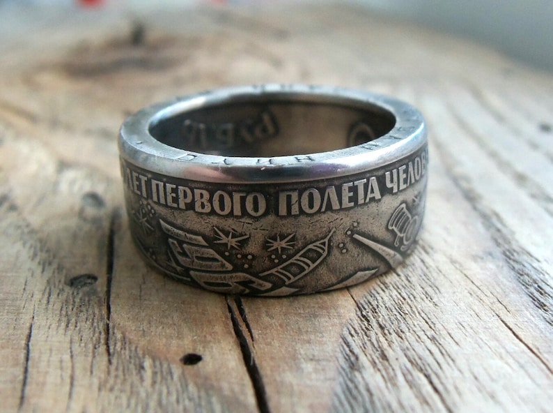 Op de afbeelding: Een zilveren ring gemaakt van een munt ter herdenking van de 50e verjaardag van de eerste bemande ruimtevlucht. De ring heeft de tekst "50 лет первого полета человека" die vertaald wordt als "50 jaar van de eerste bemande vlucht" en een afbeelding van een raket die de ruimte in wordt gelanceerd.