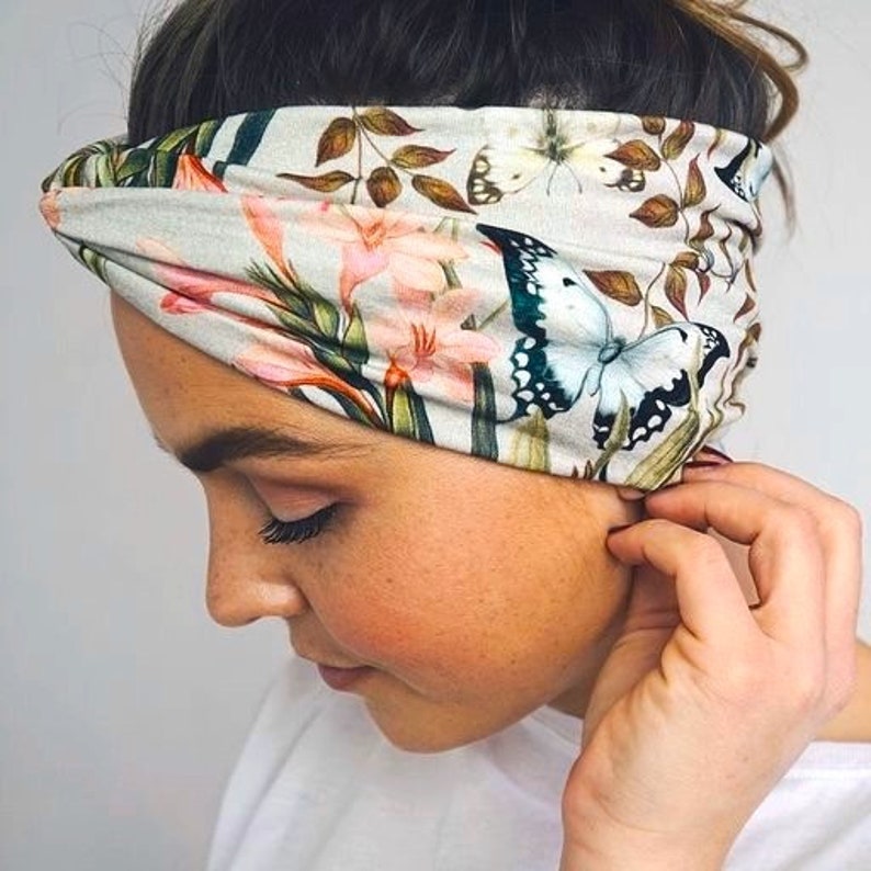 Puede incluir: Una diadema floral con mariposas y flores en tonos rosa, blanco y verde. La diadema est&aacute; hecha de una tela suave y se usa alrededor de la cabeza. El dise&ntilde;o incluye mariposas, lirios y hojas.