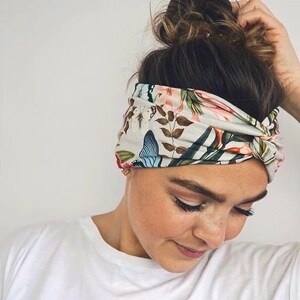 Puede incluir: Una diadema floral con dise&ntilde;o de mariposas y elementos bot&aacute;nicos. La diadema es principalmente gris claro con detalles en rosa, azul y verde. La tela est&aacute; envuelta y anudada, creando un accesorio elegante.