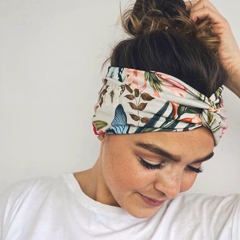 Puede incluir: Una diadema floral con dise&ntilde;o de mariposas y elementos bot&aacute;nicos. La diadema es principalmente gris claro con detalles en rosa, azul y verde. La tela est&aacute; envuelta y anudada, creando un accesorio elegante.
