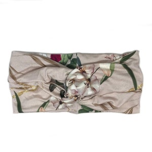 K&ouml;nnte beinhalten: Ein beiges Stirnband mit einem Blumenmuster mit rosa, wei&szlig;en und gr&uuml;nen Blumen. Das Stirnband hat ein verdrehtes Knotendesign in der Mitte und goldene Glitzerakzente.