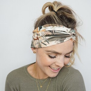 Op de afbeelding: Een brede haarband met een botanische print in groen, bruin en beige tinten. De haarband is aan de voorkant gedraaid. Dit haaraccessoire is een modieus item. De haarband is een stijlvolle toevoeging aan elke outfit.