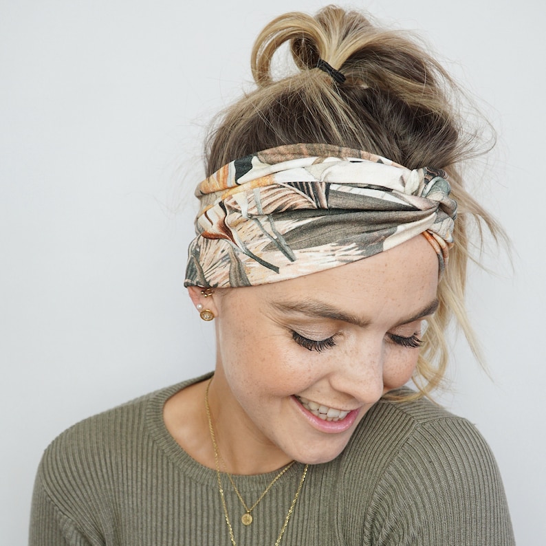 Op de afbeelding: Een brede haarband met een botanische print in groen, bruin en beige tinten. De haarband is aan de voorkant gedraaid. Dit haaraccessoire is een modieus item. De haarband is een stijlvolle toevoeging aan elke outfit.