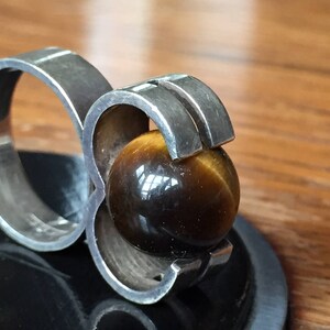 May include: A silver ring featuring a large, round, brown tiger's eye gemstone set in a geometric design.