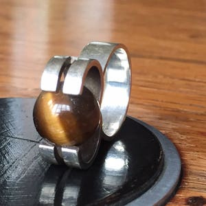 May include: A silver ring with a brown tiger's eye stone set in a modern design.