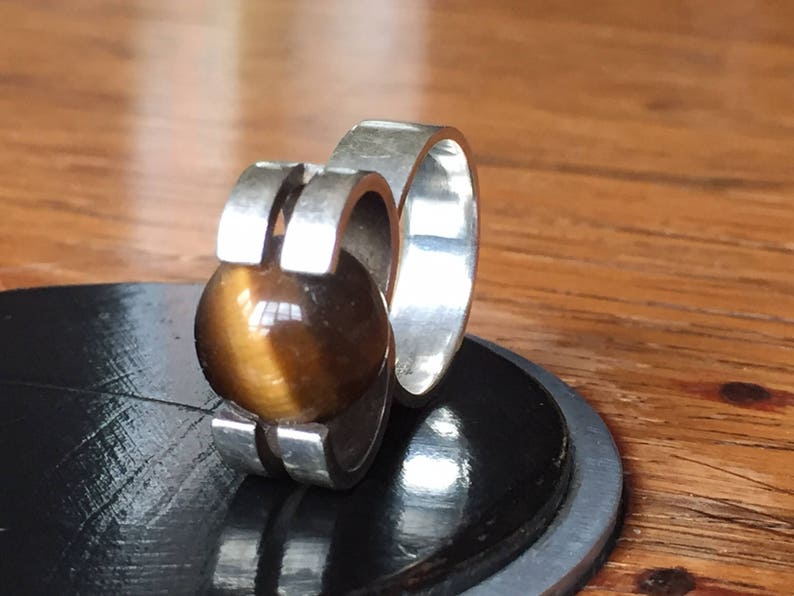 May include: A silver ring with a brown tiger's eye stone set in a modern design.