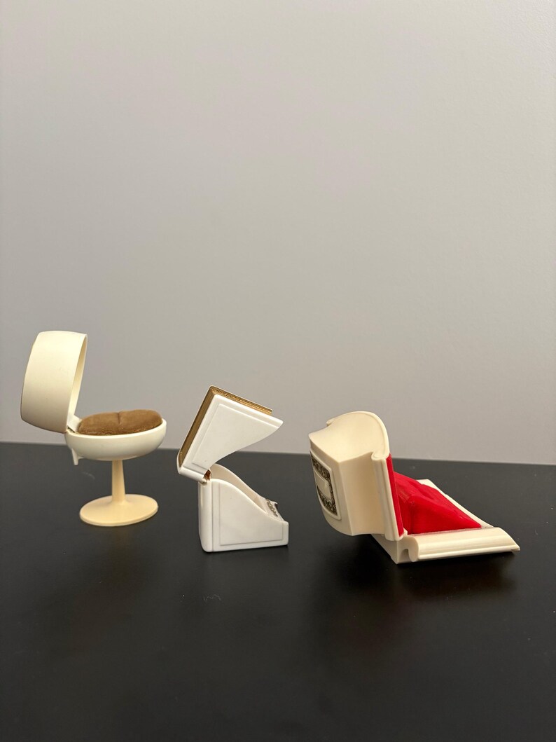 May include: Miniature ivory-colored chair with a brown seat and a small, open ivory jewelry box with a red velvet interior. Another ivory jewelry box is open, revealing a gold-colored interior.