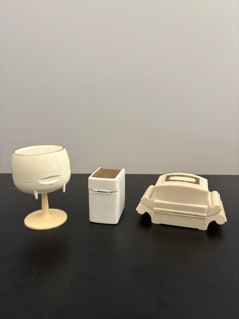 May include: Three ivory-colored decorative items: a wine glass, a small box with a gold top, and a miniature sofa. The wine glass has a rounded bowl and a pedestal base. The box is rectangular. The sofa has curved arms.