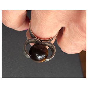May include: A silver ring featuring a brown tiger's eye stone set within a heart-shaped design.