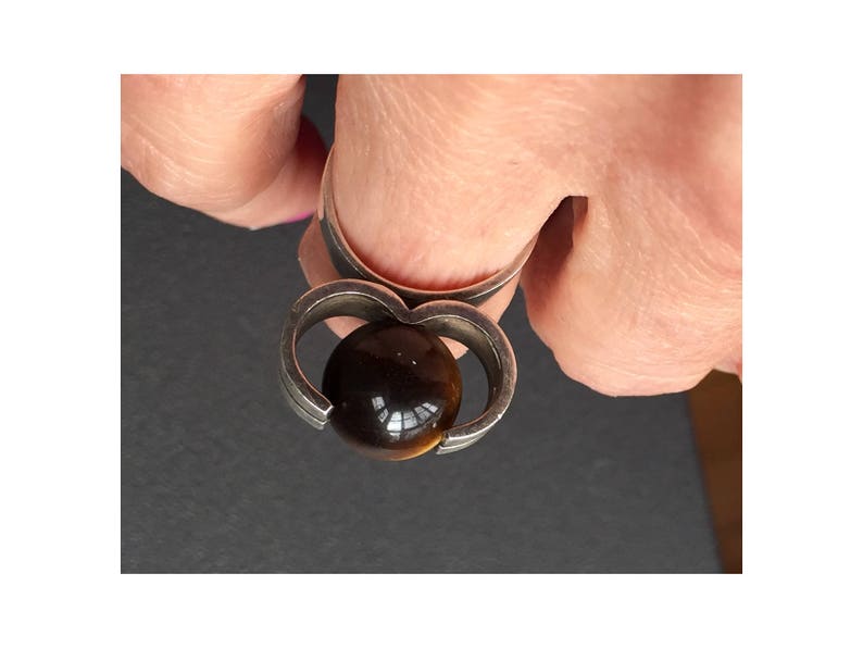 May include: A silver ring featuring a brown tiger's eye stone set within a heart-shaped design.