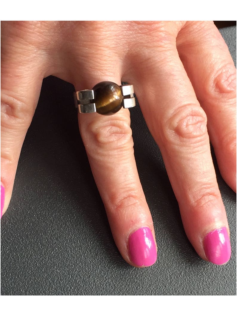 May include: A silver ring featuring a brown tiger's eye stone set in the centre. The ring has a geometric design with two silver bands on either side of the stone.