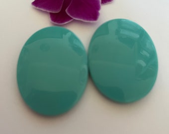 May include: Two large, oval-shaped earrings in a teal green color. The earrings are made of a smooth, glossy material.