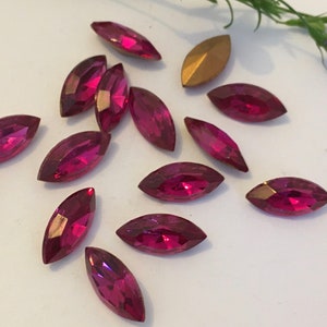May include: A scattering of maroon marquise-shaped rhinestones on a white surface.
