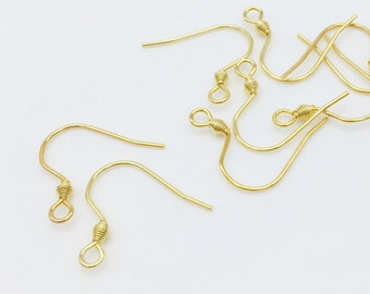 May include: A group of gold-colored earring hooks, scattered on a white surface.