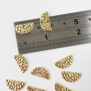 May include: Eight gold-toned metal half-circle charms with a hammered texture and two holes. The charms are approximately 1 inch in diameter.