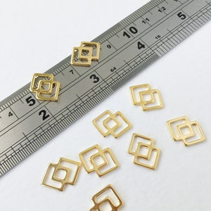 May include: Eight gold-colored metal charms in the shape of a square with a smaller square inside. The charms are arranged on a white surface with a ruler in the background.